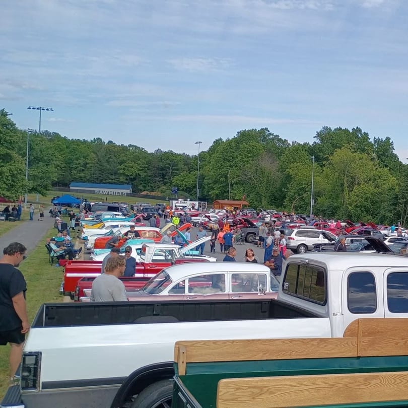 Large outdoor car show with many classic cars and people on a grassy field.