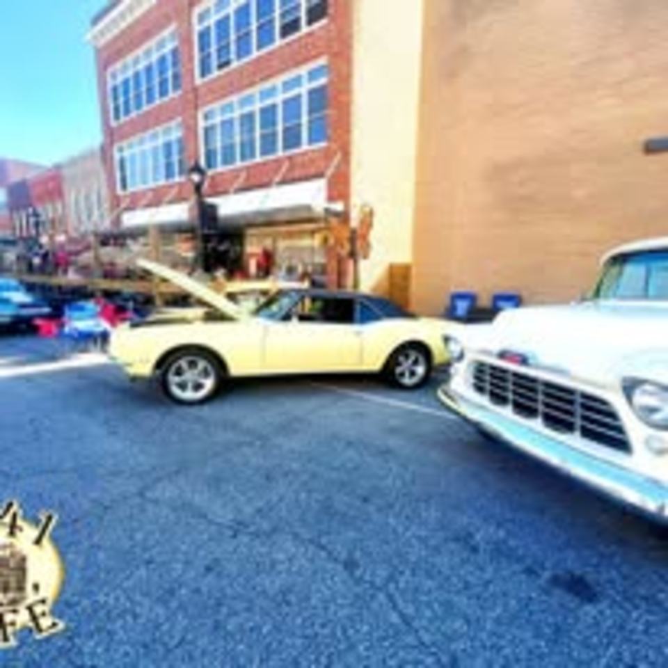 Classic cars parked on a street in front of brick buildings, with the 1841 Cafe logo.