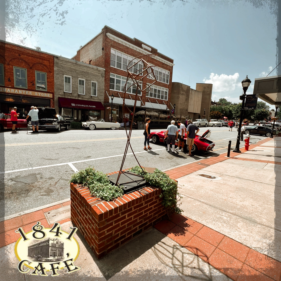 A street view of 1841 Cafe with classic cars and people on a sunny day.