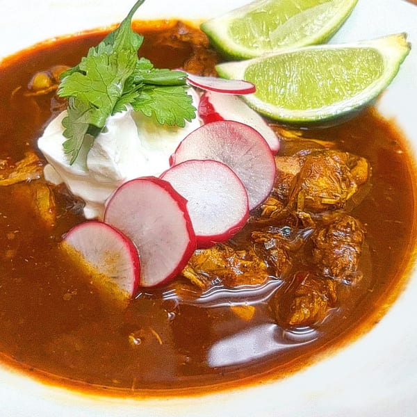 Hearty stew with meat, topped with sour cream, cilantro, sliced radishes, and lime wedges.