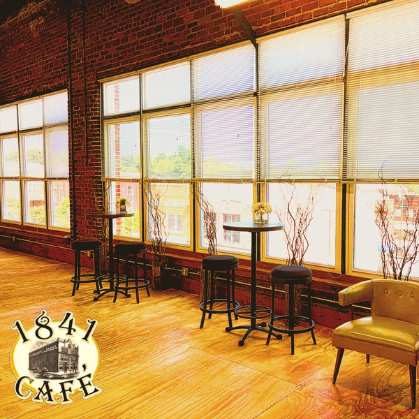 Interior of 1841 Cafe with brick walls, large windows, high-top tables, stools, and a yellow armchair.