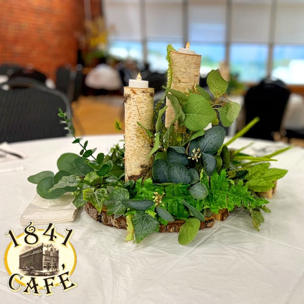 Table centerpiece with birch logs, candles, and various green foliage, at 1841 Cafe.