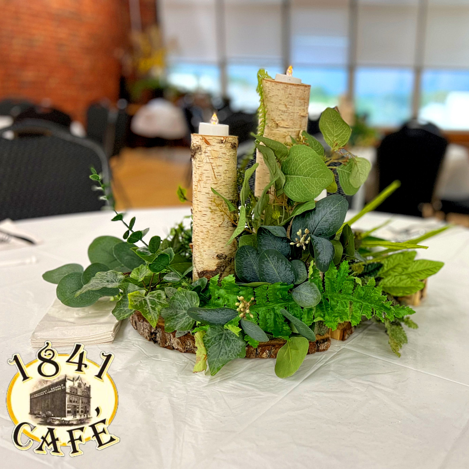 Table centerpiece with birch logs, candles, and various green foliage, at 1841 Cafe.