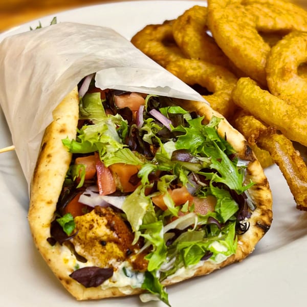 A chicken gyro wrapped in paper with lettuce, tomatoes, and onions, served with onion rings.
