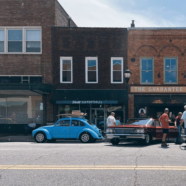 Vintage cars parked on a street in front of brick buildings with people walking around.