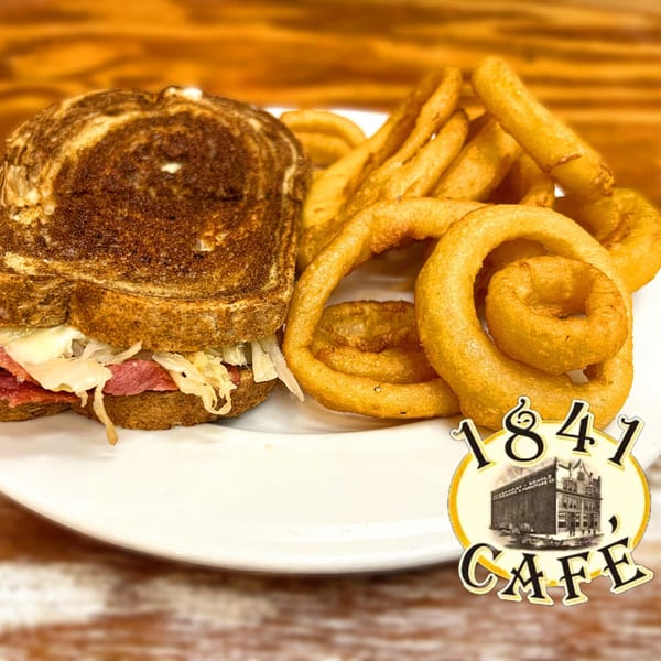 Reuben sandwich with corned beef, Swiss cheese, and sauerkraut, served with a side of onion rings.