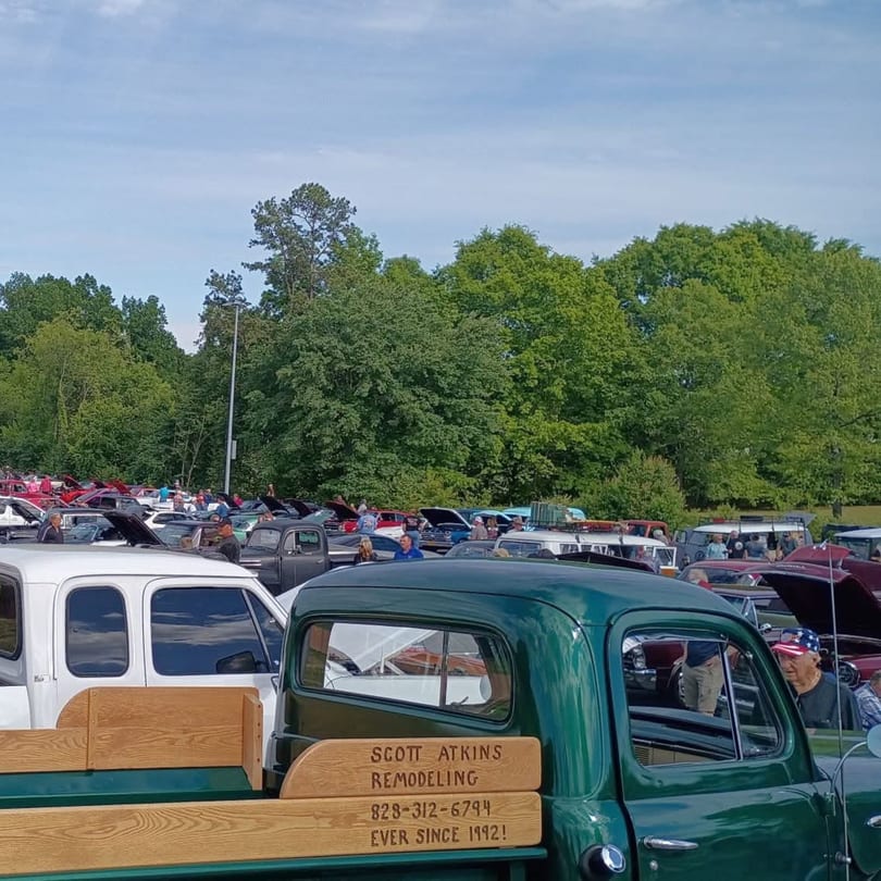 A car show with many classic cars and people, featuring a green pickup truck in the foreground.