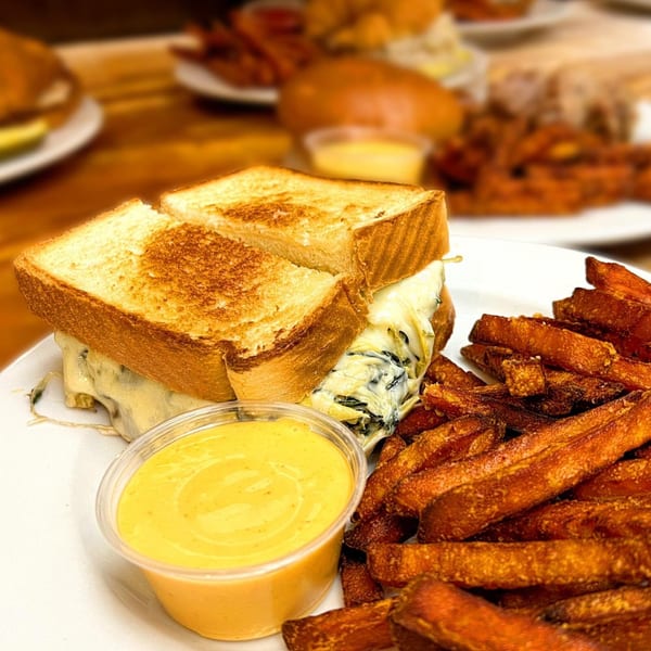 A grilled cheese sandwich with melted cheese and spinach, sweet potato fries, and dipping sauce.