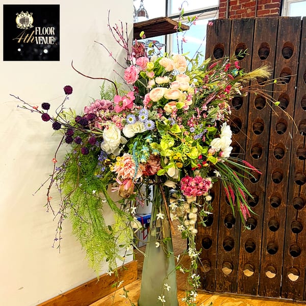 Large floral arrangement with pink, white, and purple flowers in a green vase at 1841 Cafe.