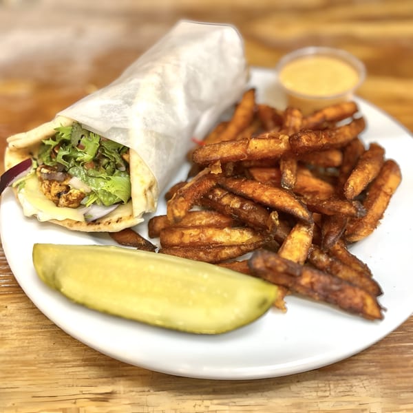 A chicken pita wrap with lettuce, onions, and cheese, served with sweet potato fries and a pickle.