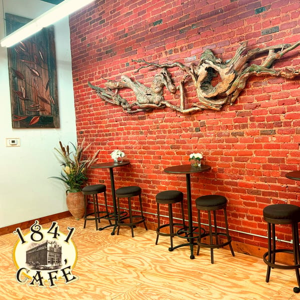 High-top tables and stools against a red brick wall with decorative wood, 1841 Cafe logo on the floor.