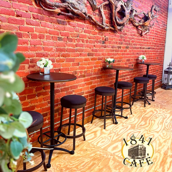 Tall tables with stools line a brick wall adorned with wooden art at 1841 Cafe.
