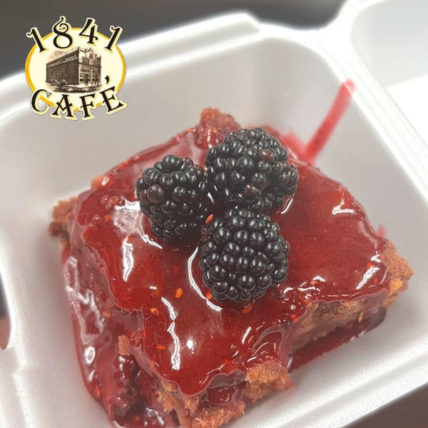 A square dessert from 1841 Cafe, topped with red glaze and three fresh blackberries.