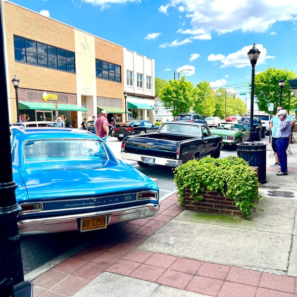 Classic cars parked on a street in front of 1841 Cafe and other businesses on a sunny day.