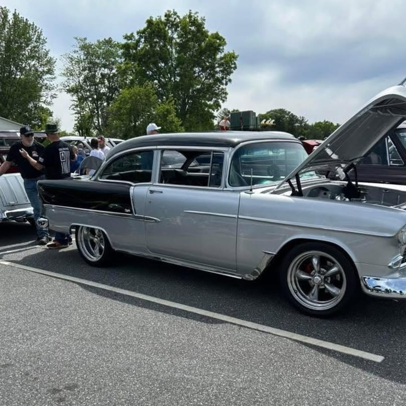 Classic silver and black car with open hood at an outdoor car show with people.