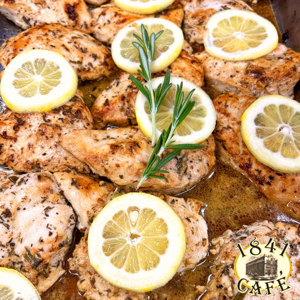 Grilled herb-seasoned chicken pieces arranged with lemon slices and fresh rosemary in a savory pan sauce.