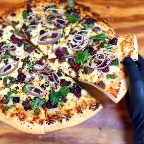 A hand in a black glove lifts a slice of 1841 Cafe's pizza with red onions and basil.