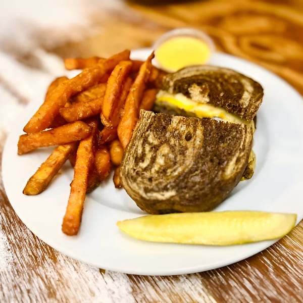Grilled cheese sandwich with sweet potato fries, a pickle spear, and dipping sauce on a white plate.