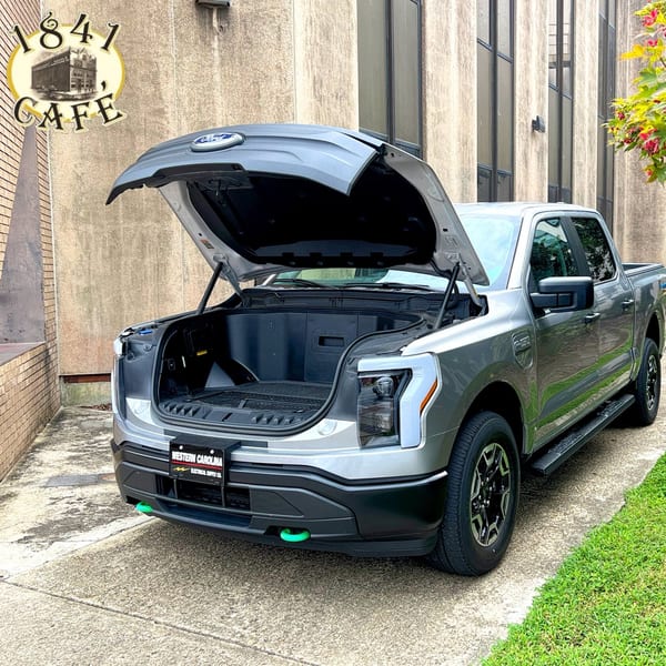 A silver Ford F-150 Lightning truck with its hood open, parked outside 1841 Cafe.