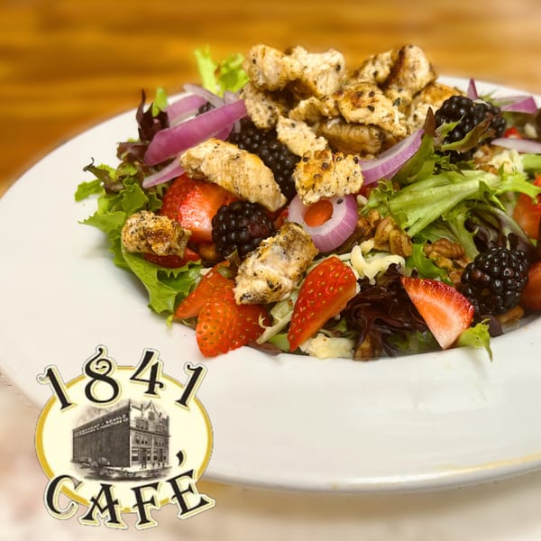 A vibrant salad with grilled chicken, mixed greens, strawberries, blackberries, red onion, and walnuts.