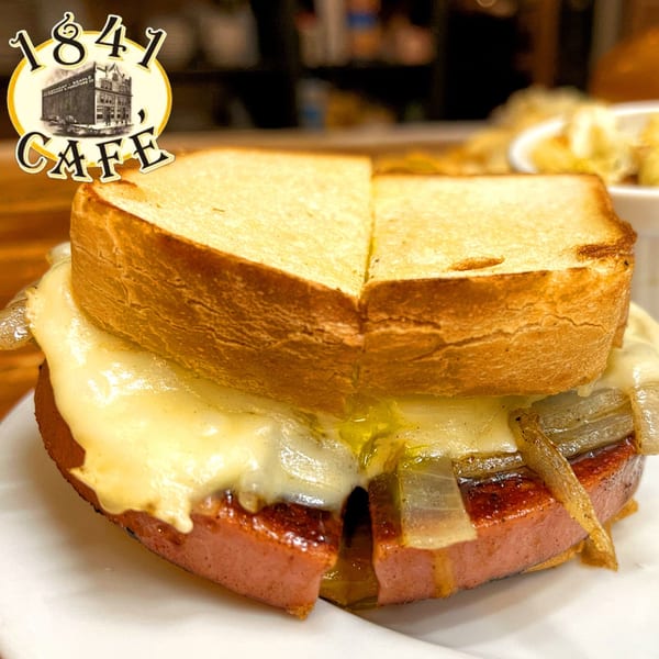 A close-up of a grilled bologna sandwich with melted cheese and caramelized onions on toasted bread.