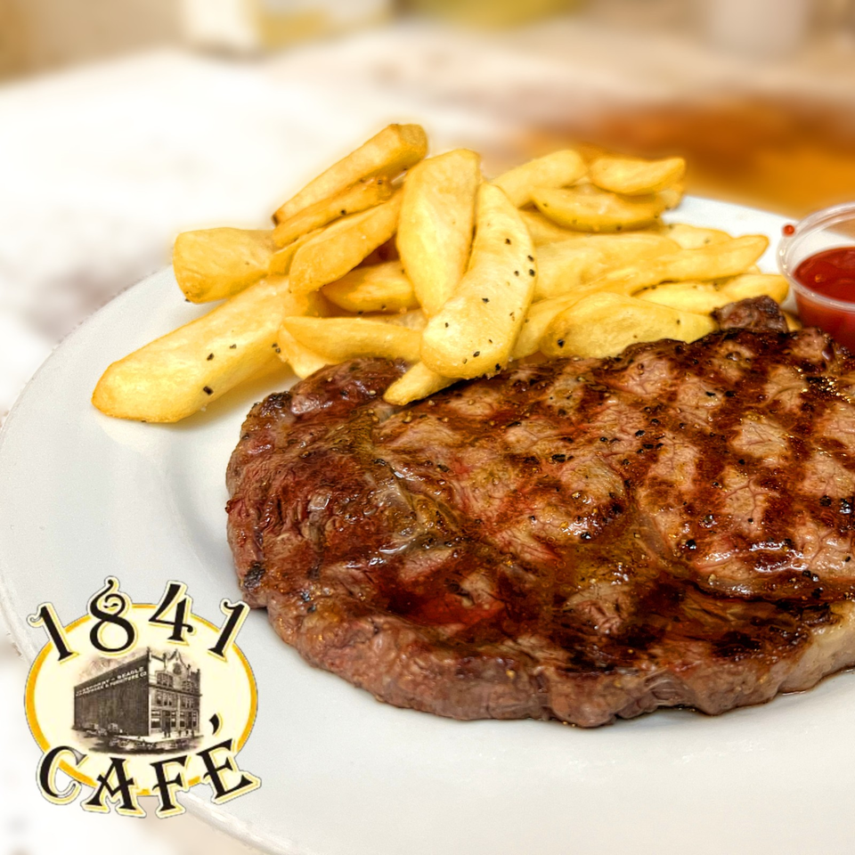 Grilled steak served with seasoned fries and ketchup on a white plate at 1841 Café.