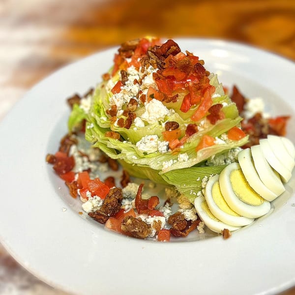 A wedge salad with blue cheese, bacon, tomatoes, and sliced hard-boiled eggs on a white plate.