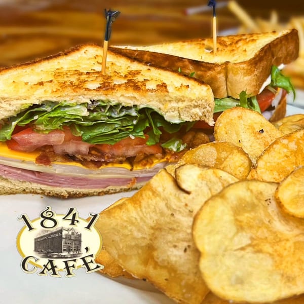 A grilled club sandwich with lettuce, tomato, cheese, and meat, served with potato chips.