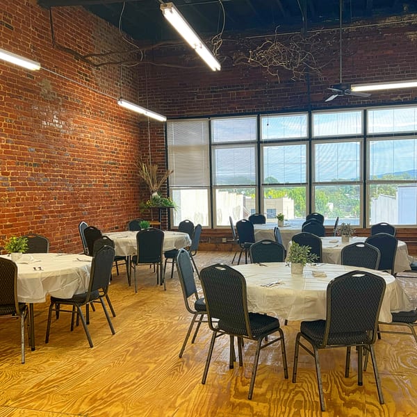 An empty dining room at 1841 Cafe with round tables, chairs, brick walls, and large windows.