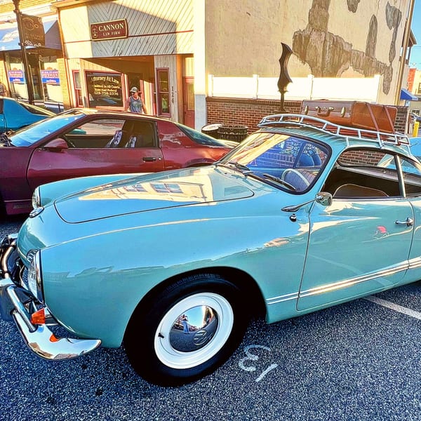 A light blue vintage car with a luggage rack and suitcase parked on a street.