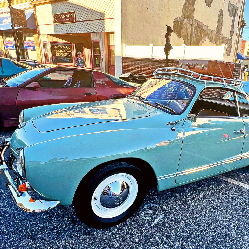 A light blue vintage car with a luggage rack and suitcase parked on a street.