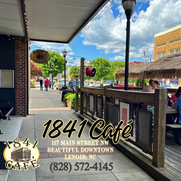 Outdoor patio of 1841 Cafe with people dining under thatched umbrellas on a sunny day.